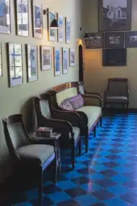 Salon élégant aux murs verts, mobilier ancien capitonné vert, sol carrelé bleu et une riche galerie d'art mural.